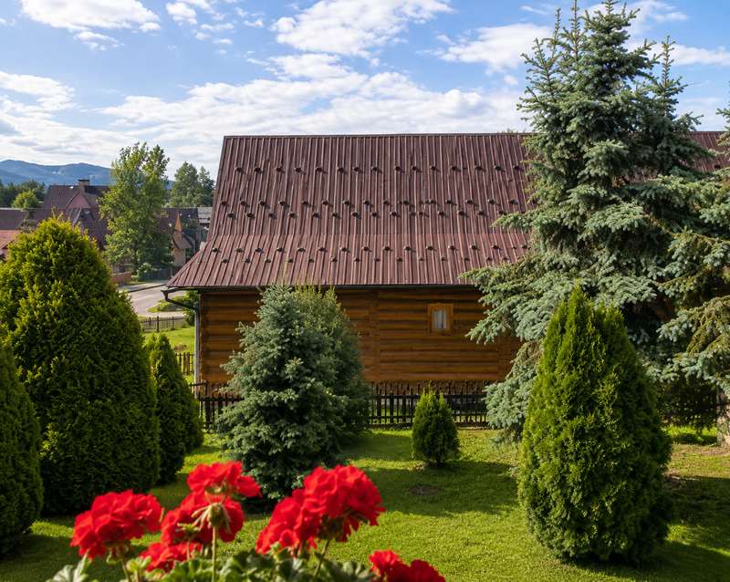 Ogród z przystrzyżonymi iglakami, pelargoniami i miejscem do siedzenia