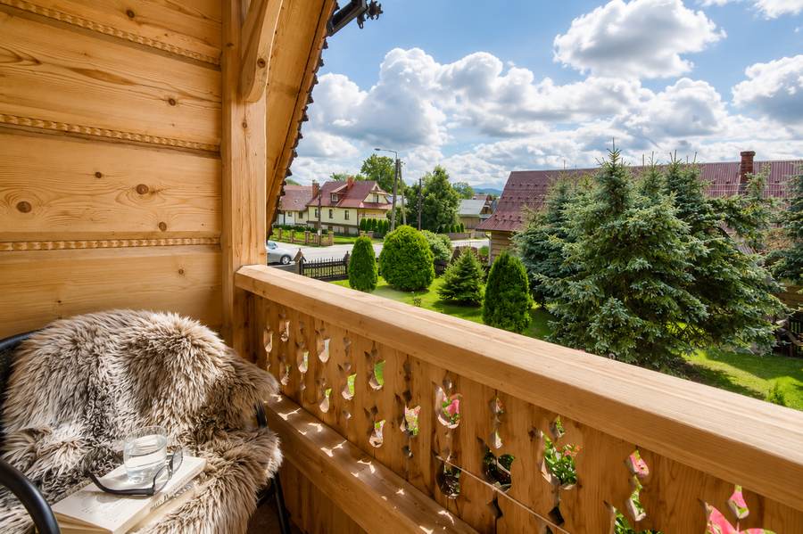 Rzeźbiony drewniany balkon z fotelem nakrytym owczą skórą i widokiem na ogród
